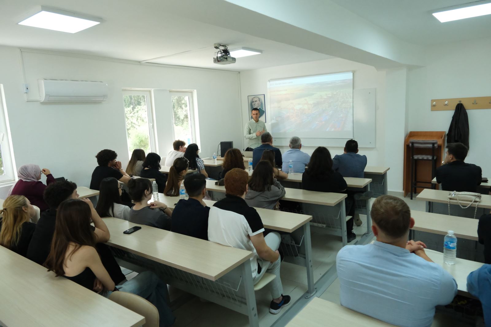 During the talk held in the classroom, the speaker is giving a presentation whilst students and participants sit in rows, following the event.